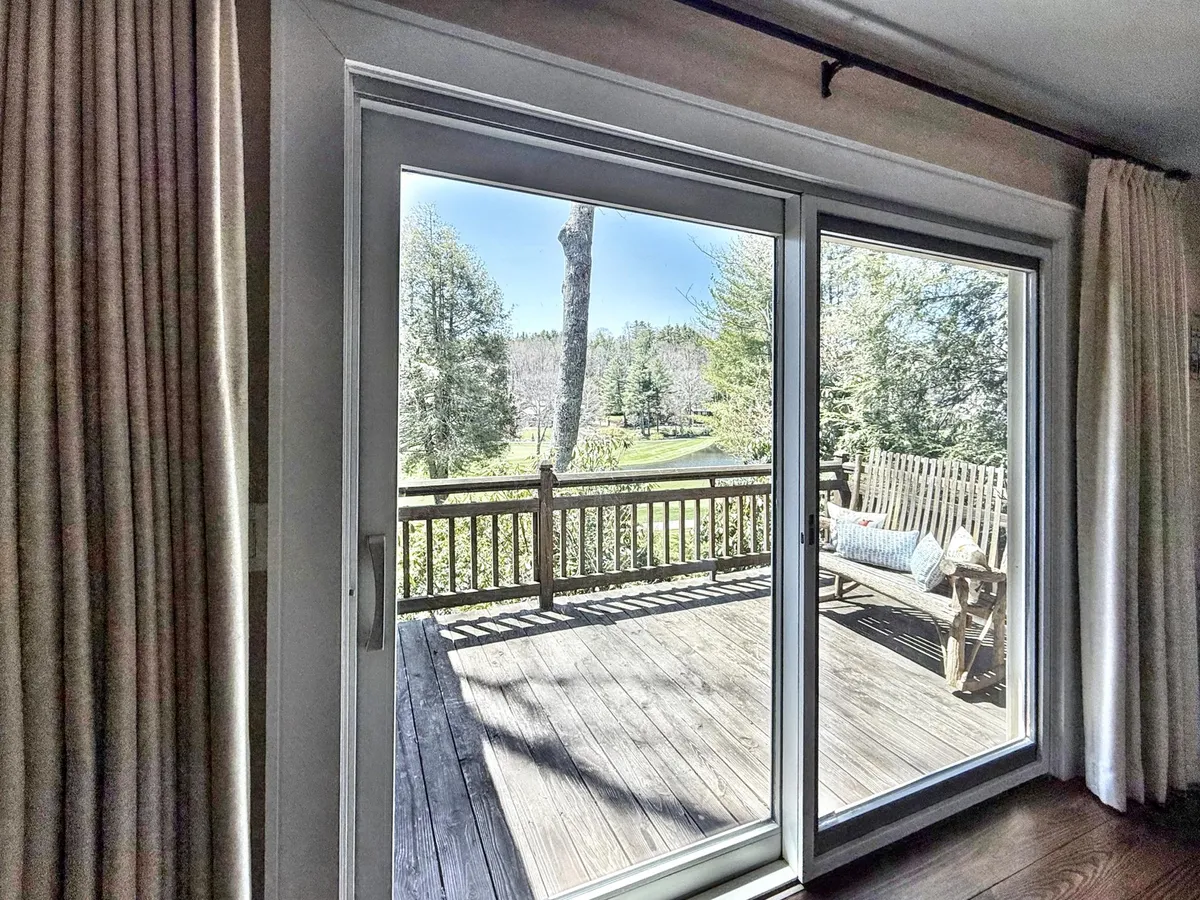 A sliding glass door opens directly onto a wooden deck with a bench, surrounded by lush greenery. The space invites seamless transitions between indoors and out, ideal for hosting, relaxing, or enjoying mountain sunsets.