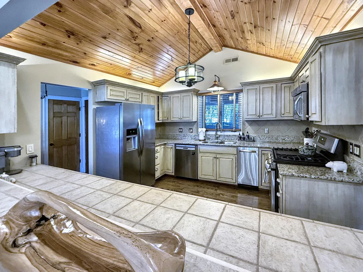 A warm, inviting kitchen featuring granite countertops, stainless steel appliances, a decorative light fixture, and a rich wooden ceiling. The space is designed for both cooking and entertaining, with ample workspace and high-end finishes that promise memorable meals.
