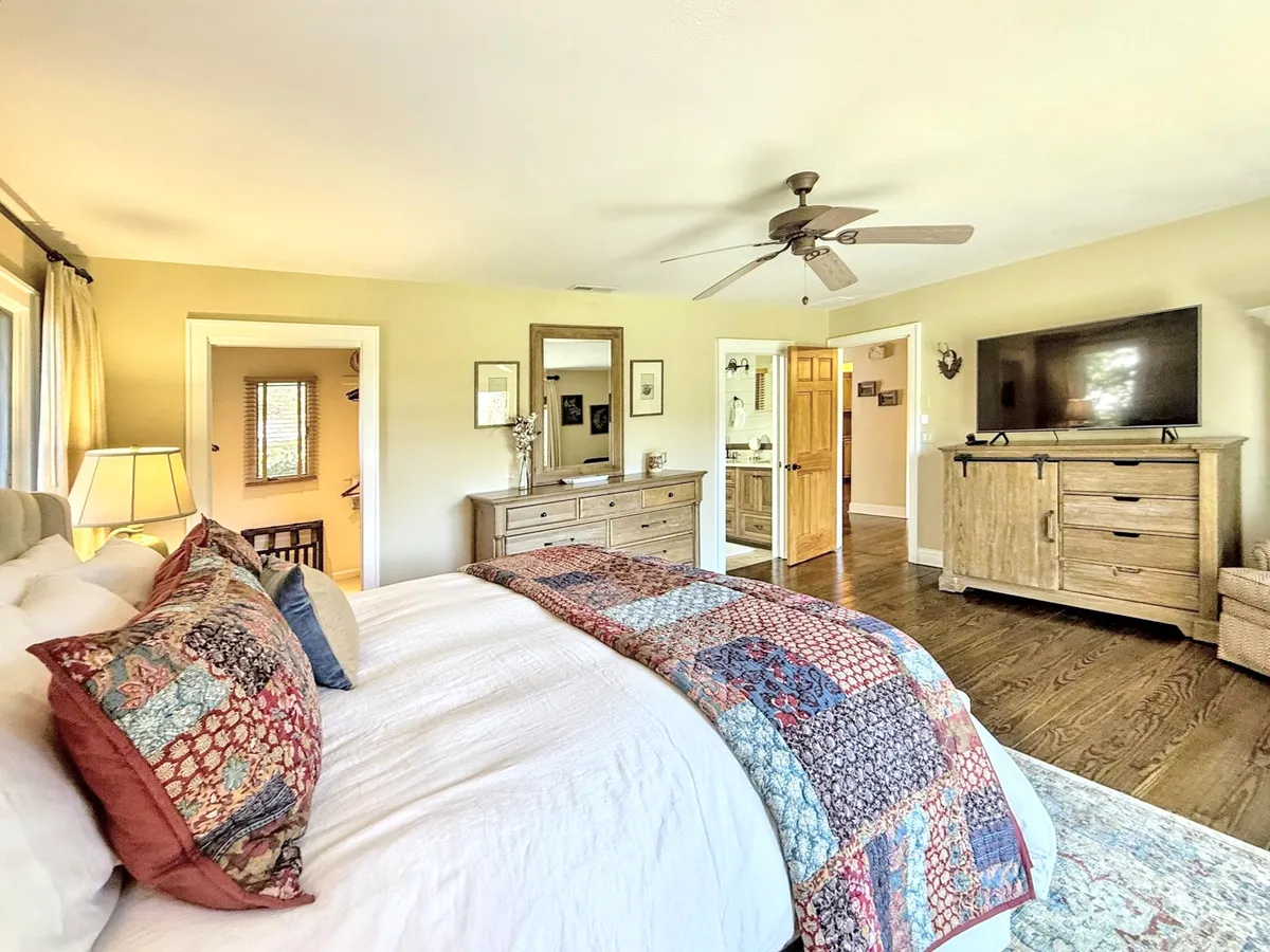 A welcoming guest bedroom featuring a bed covered with a colorful quilt, a wooden dresser for ample storage, and a wall-mounted TV. The room exudes warmth and comfort, inviting guests to relax, read, or watch TV in their own private space.