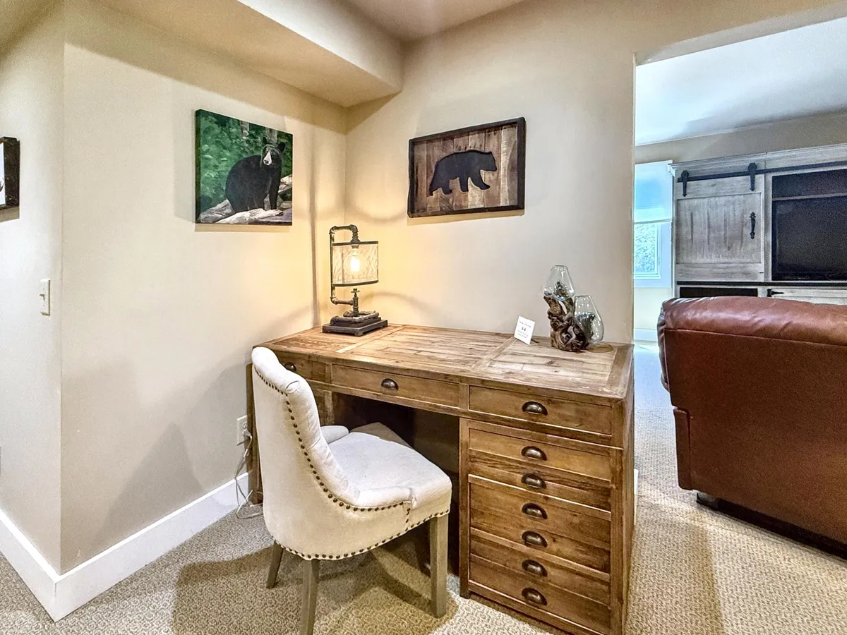 A cozy wooden desk set in a warm, inviting corner, complemented by bear-themed artwork and a glowing table lamp. The setting is both practical and inspiring, ideal for productive work or creative sessions in a serene environment.