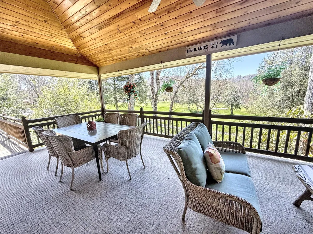 A peaceful outdoor space with a dining table, comfortable sofa, hanging plants, and a wooden ceiling, set up for both meals and relaxation. The area overlooks lush scenery, inviting guests to enjoy sunset views and gentle breezes while being sheltered from the elements.