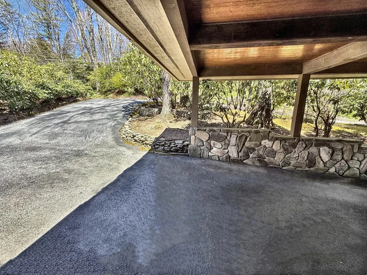 An exterior view featuring a stone wall, wooden beams, and a driveway leading up to the porch. The tranquil mood invites guests to imagine returning from a day exploring local markets to relax in their private oasis.