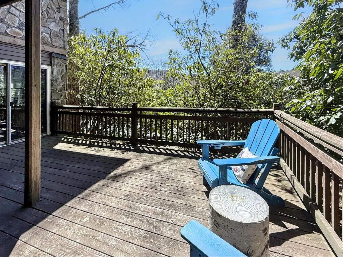 A serene wooden deck is adorned with a blue Adirondack chair, surrounded by lush green foliage and a rustic stone wall. The space invites relaxation and offers glimpses of outdoor tranquility.