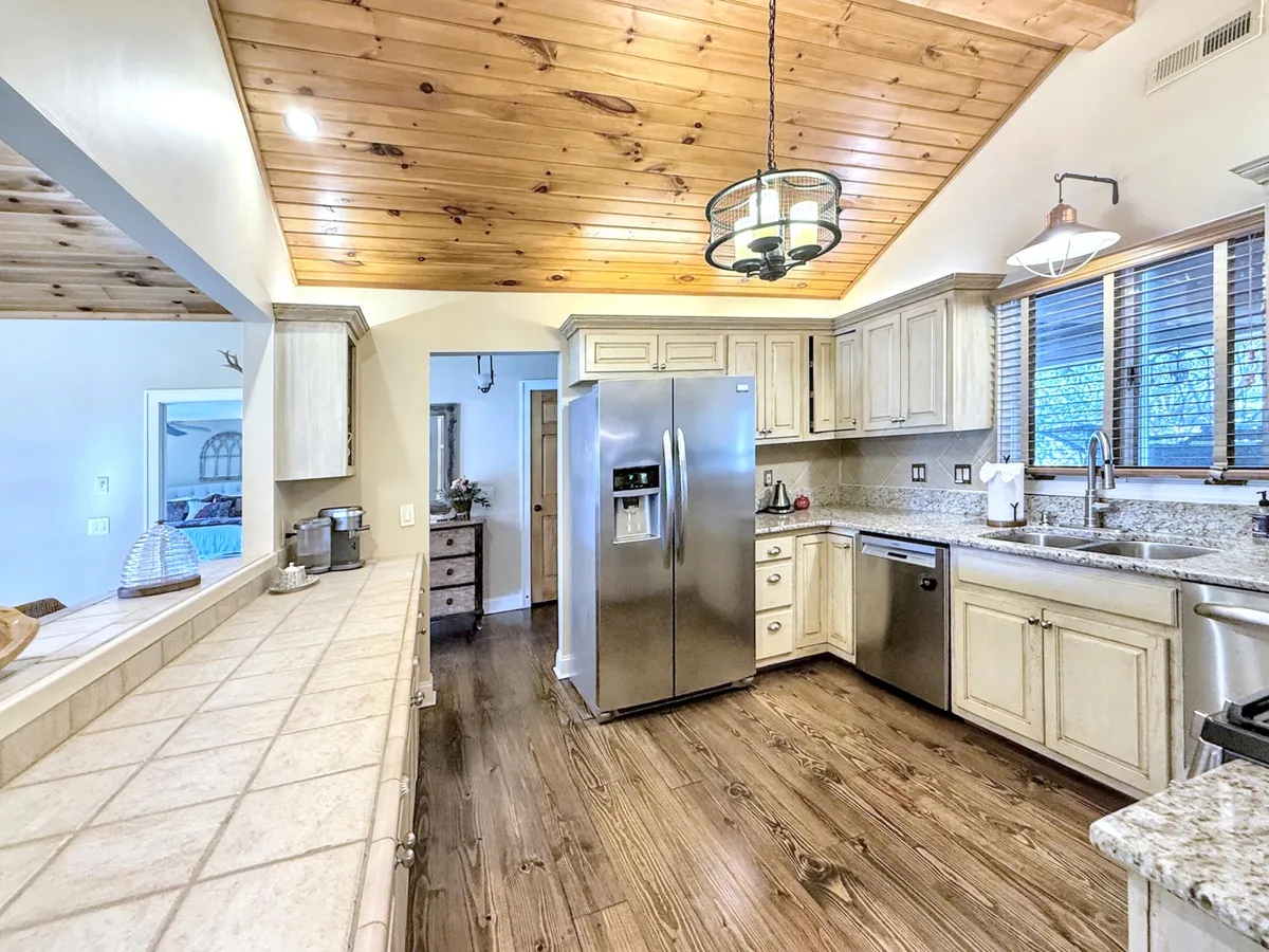 A spacious kitchen with a prominent kitchen island, stainless steel refrigerator, granite countertops, and wooden ceiling. The layout invites group cooking sessions or casual gatherings, highlighting the home's suitability for entertaining and shared meals.