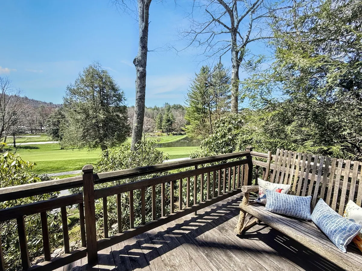 A tranquil outdoor sitting area with a wooden bench and decorative pillows, surrounded by lush greenery and offering an expansive view over the golf course and mountains. The setting is ideal for morning coffee or relaxing afternoons, with the blue sky enhancing the serene mood.