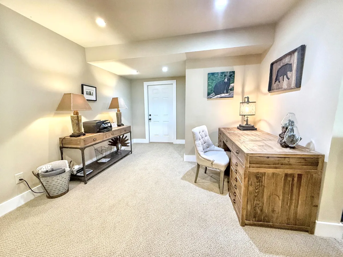 A cozy office area featuring a wooden desk, lamps, and artwork with bear motifs on light-colored walls. The setup includes a comfortable workspace ideal for productivity.