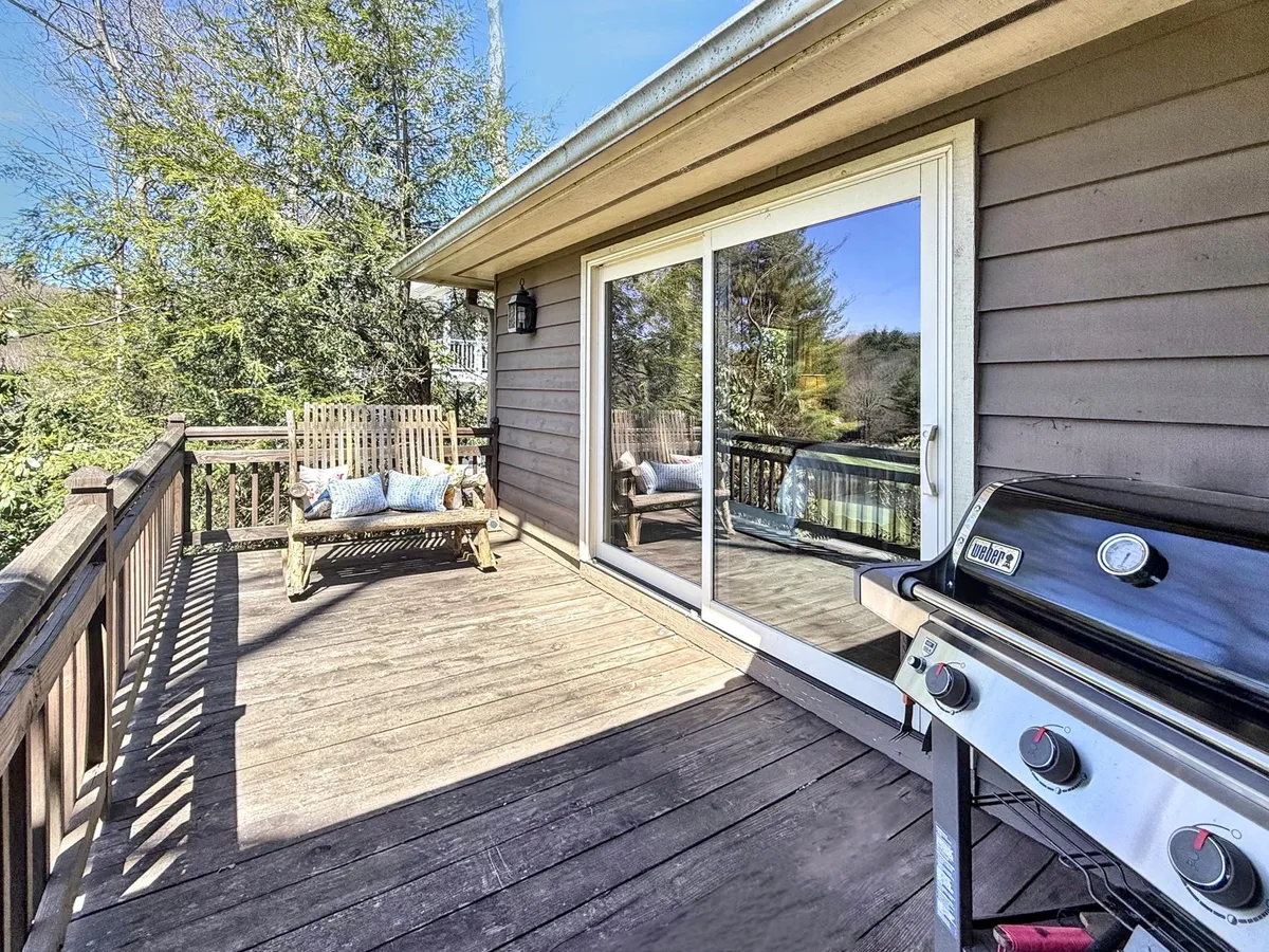 This image displays the exterior of the retreat with a wooden bench swing, a grill, and a sliding glass door, suggesting an inviting patio area perfect for outdoor dining or relaxing. The setting is casual yet charming, with views of nature just beyond the patio.