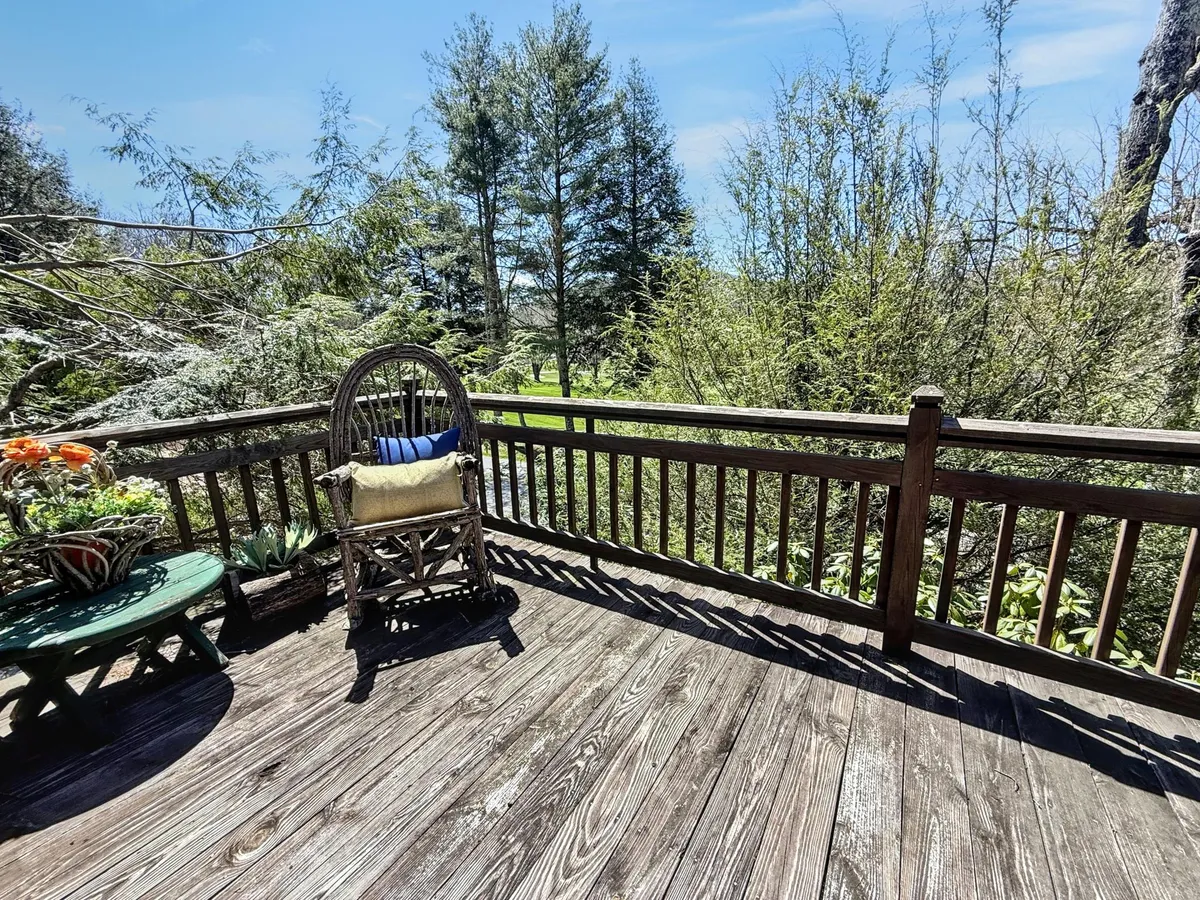 A peaceful outdoor wooden deck featuring a classic rocking chair and potted plants, surrounded by lush greenery. The inviting setup suggests a perfect spot for relaxing, birdwatching, or simply taking in the changing seasons in the fresh mountain air.