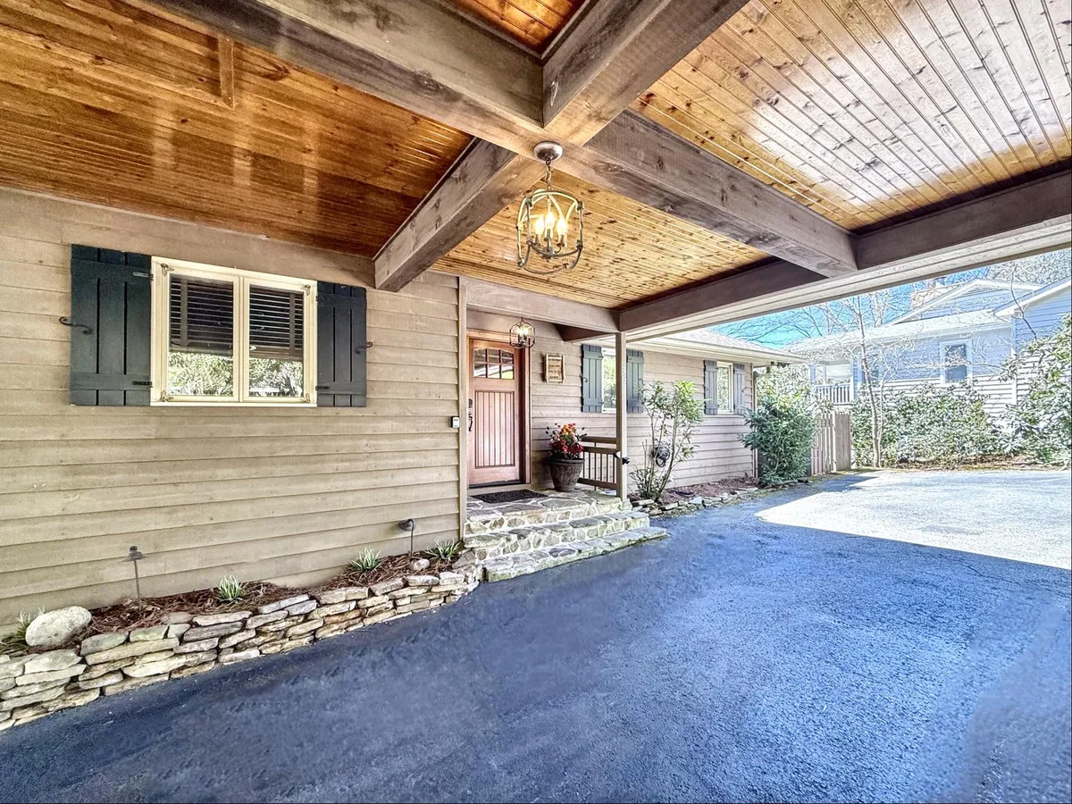 This image shows the inviting front entrance of a house, featuring a stone pathway leading to a wooden front door with a hanging lantern. The exterior is accented with shuttered windows and lush garden plants, creating a welcoming and picturesque first impression.