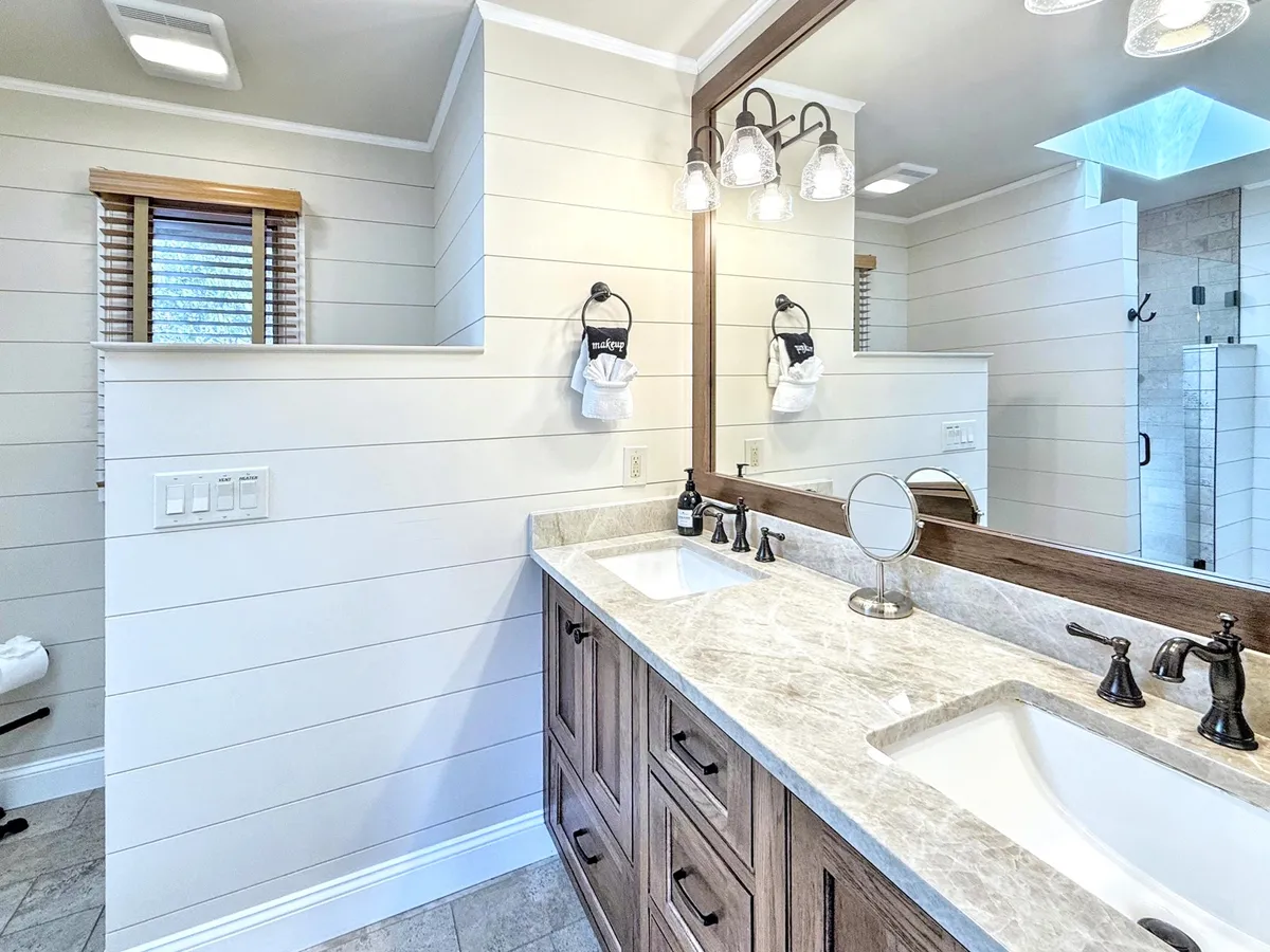 A luxurious, spa-inspired ensuite bathroom with a double vanity, large mirror, and elegant lighting fixtures. The overall look is clean, tranquil, and perfect for self-care routines or moments of relaxation.