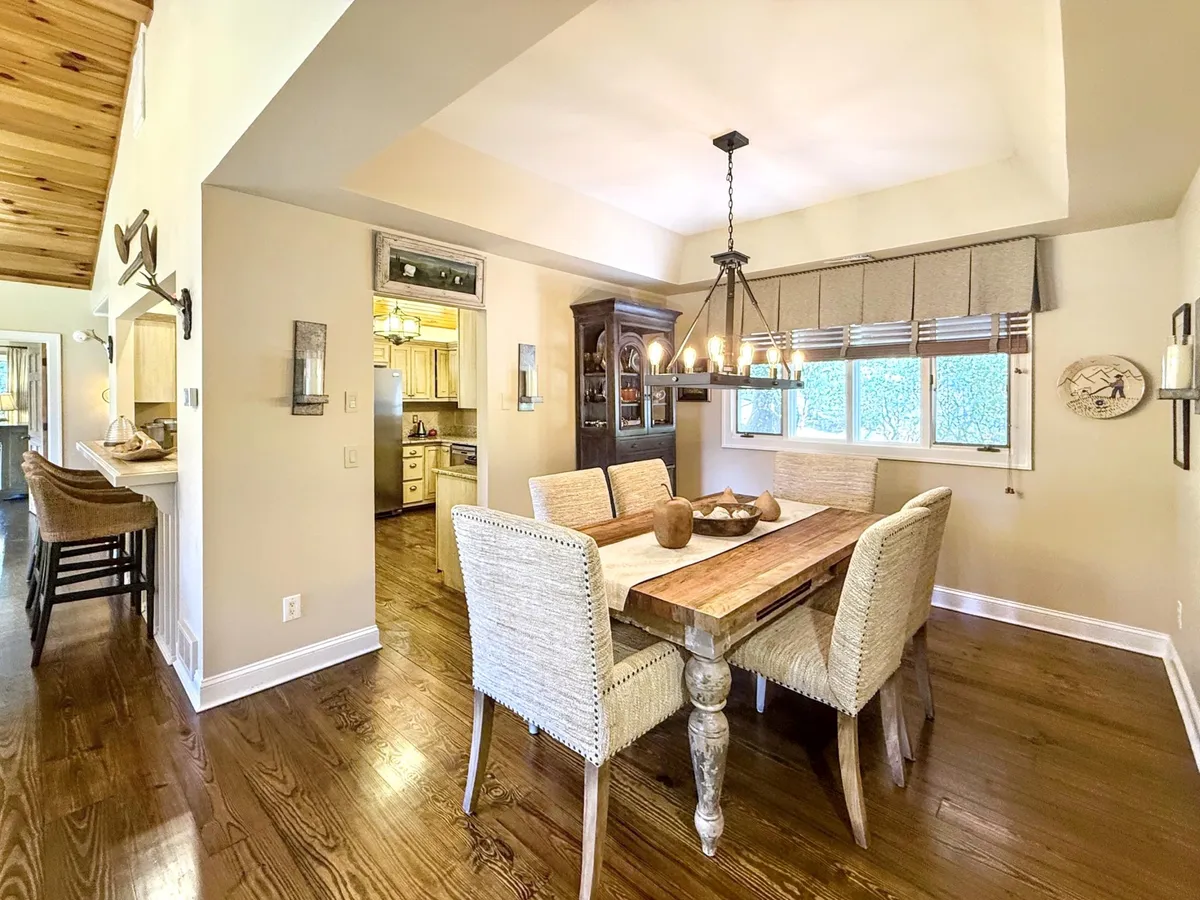 An elegant dining area featuring a central dining table, a modern chandelier above, and large windows that fill the space with natural light. The room is set for family dinners, celebrations, or casual brunches, offering a view that enhances mealtime ambiance.