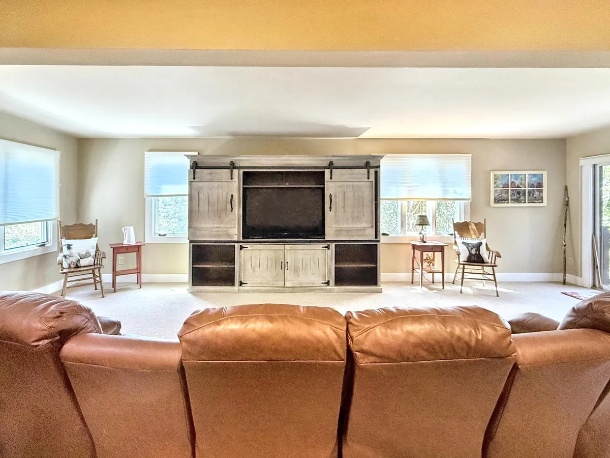 A cozy entertainment room featuring a brown leather couch facing an entertainment center, flanked by comfortable side chairs. The seating arrangement invites groups to gather and enjoy movies or games in a relaxed atmosphere.