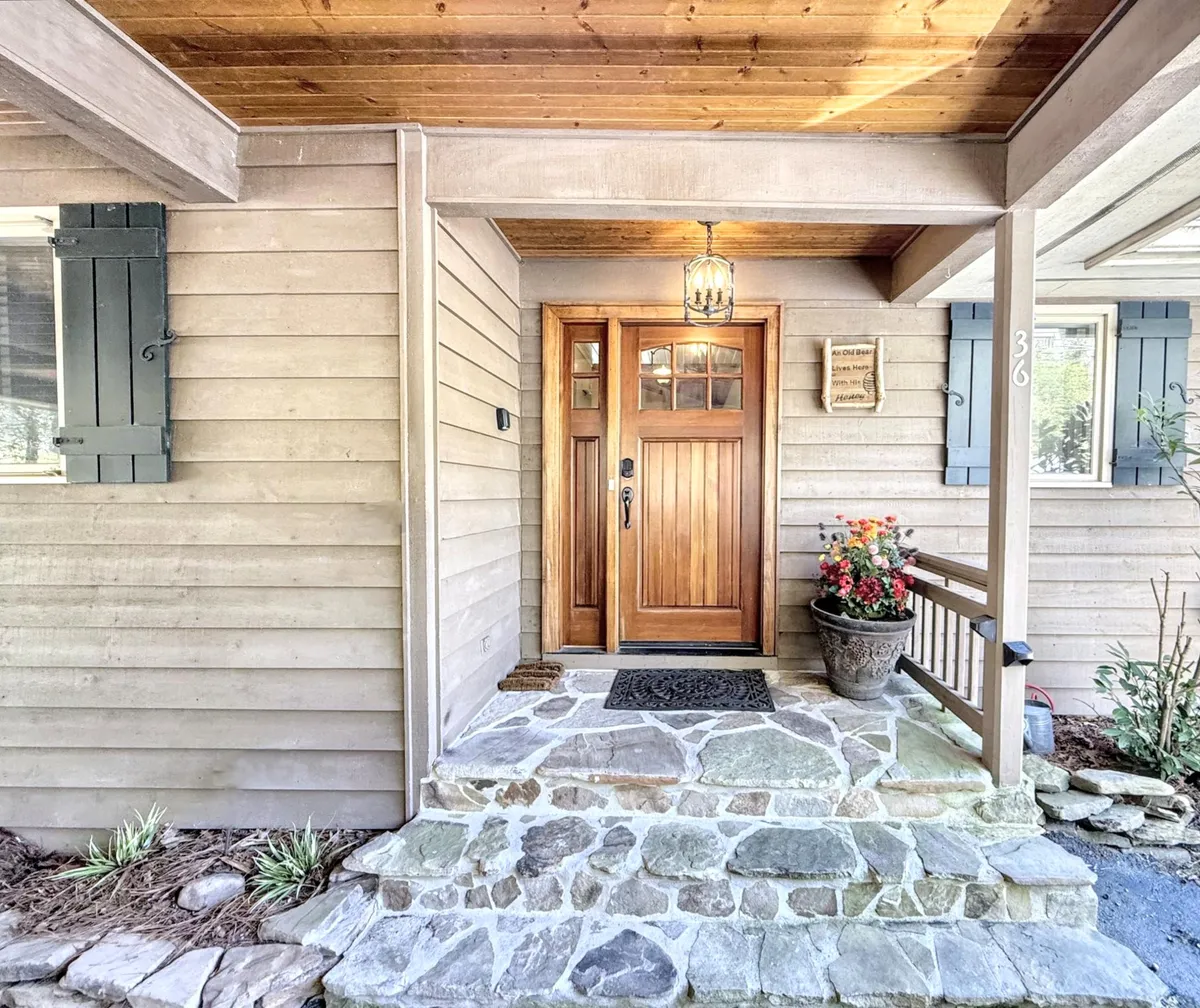 The image features a cozy front door with a stone pathway, a hanging lantern above the entrance, and a decorative flower pot, all set against an inviting and well-kept exterior facade.